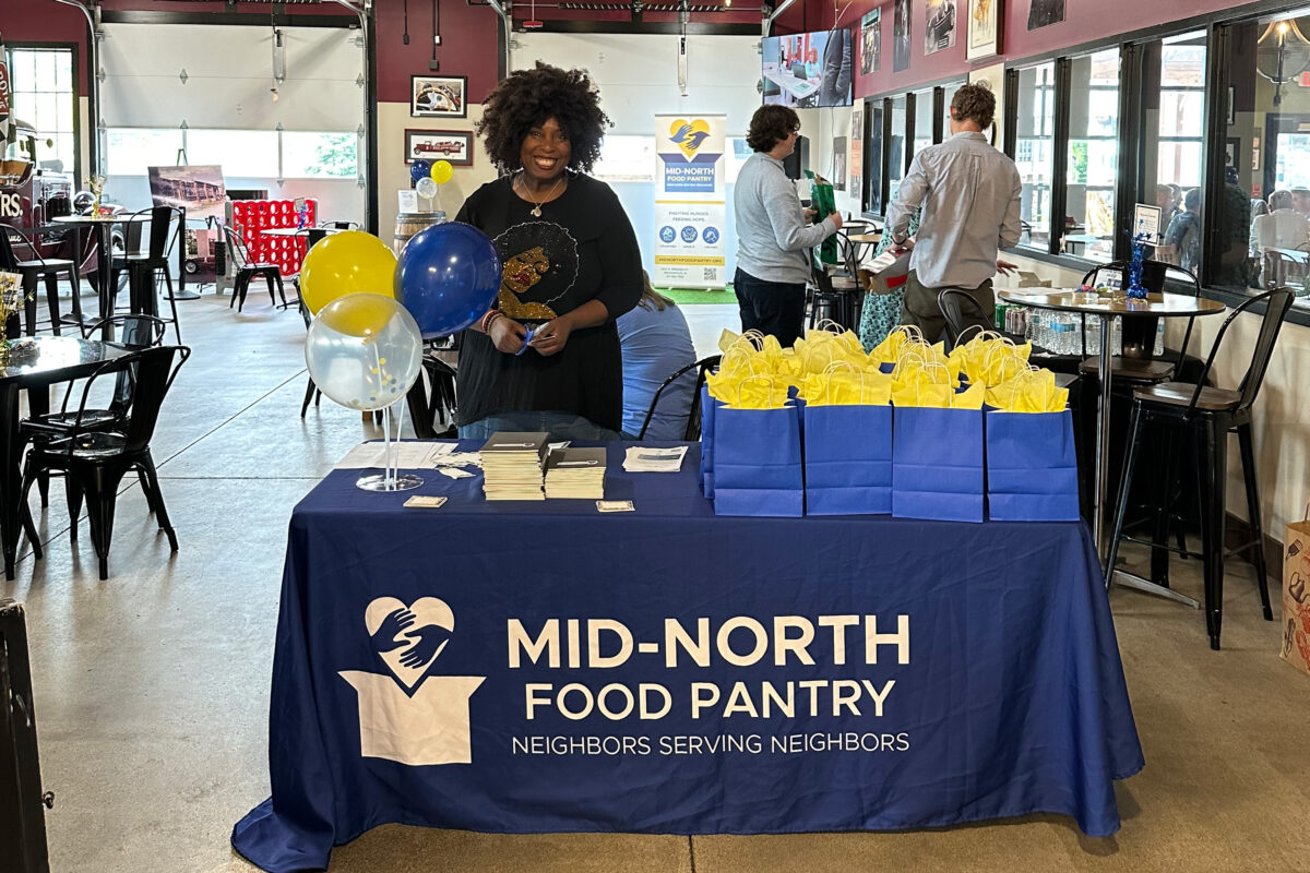 A volunteer standing behind a Mid-North Food Pantry table at an event