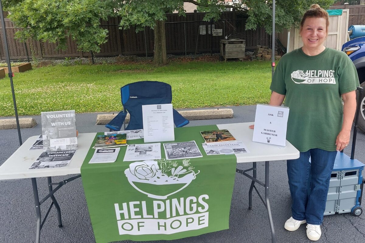 A Helpings of Hope volunteer standing next to a table with information.